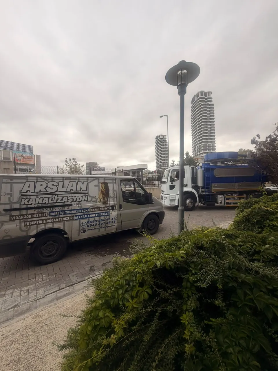 Arslan servis aracı ile vidanjör aracı aynı çalışma noktasında, arkada yüksek konut kuleleri